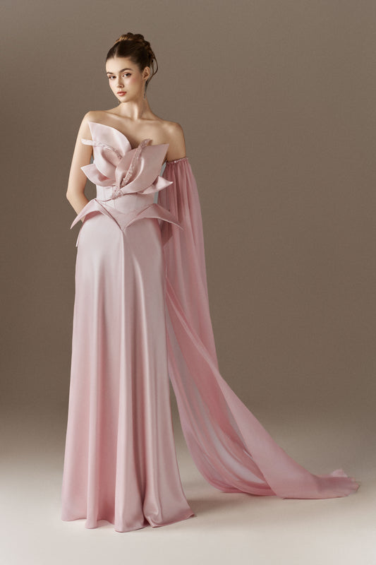 A vibrant  figure-hugging maxi dress with a bandeau neckline. The dress features a large 3D floral bust detail adorned with crystals, and a detachable single cape sleeve on the left arm.