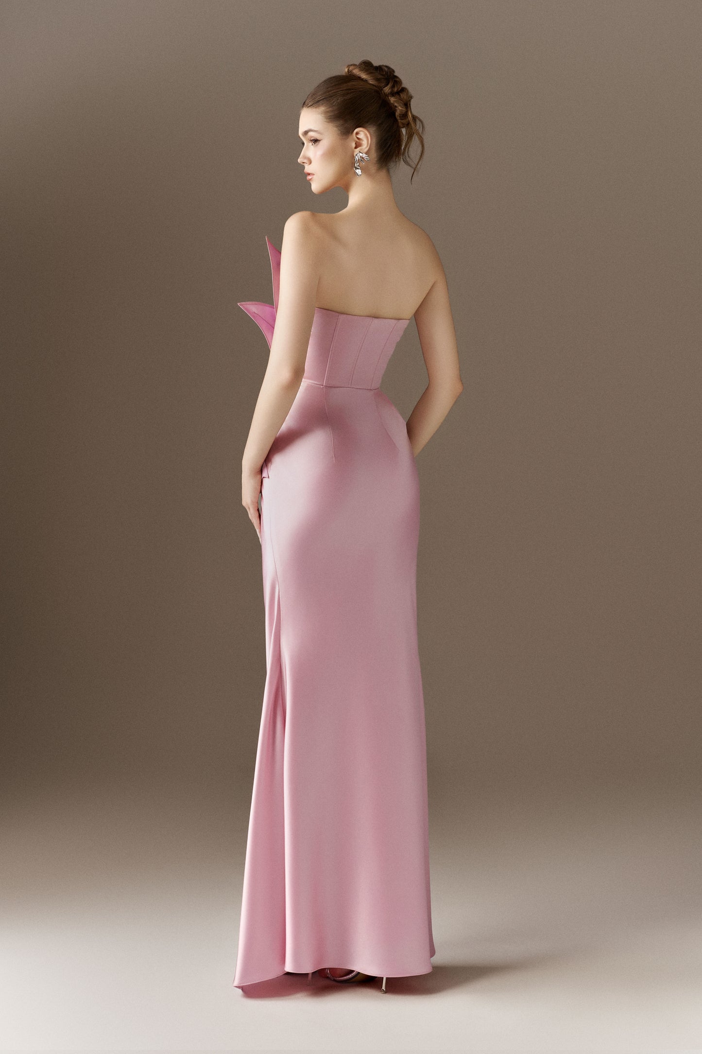 The back view of a pink, figure-hugging maxi dress, showcasing its flowing silhouette and the off-shoulder open neckline from behind.